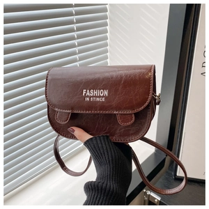Detail of dark brown vintage saddle bag featuring oily leather texture and white lettering