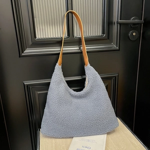 Light blue faux shearling tote bag with brown leather strap hanging on a door handle