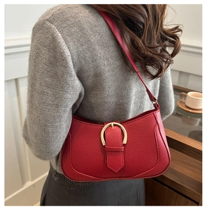 Red pebbled leather shoulder bag with gold horseshoe buckle detail on model shoulder