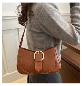 Detail of brown lychee grain leather crescent bag with gold horseshoe buckle on model