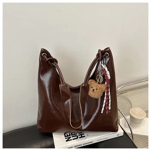 Detail of vintage brown leather tote bag with plush bear charm and ribbon decor