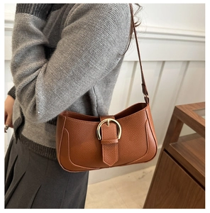 Close-up of brown litchi pattern leather shoulder bag with golden buckle on a model