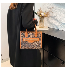 Detail of leopard print tote bag featuring orange handles and gold zipper pocket accent