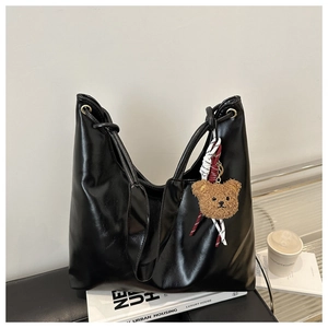 Detail of a black leather tote bag with a cute brown plush bear charm on a soft bench