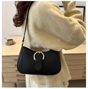 Detail of black pebbled leather shoulder bag featuring a gold horseshoe metal buckle