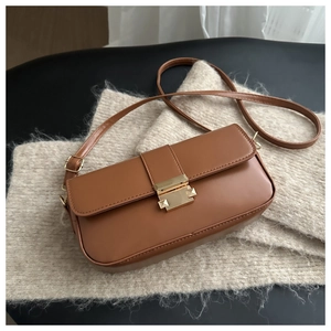 Detail of caramel brown leather crossbody bag with golden rectangular clasp and strap