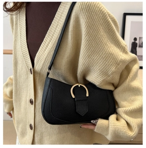 Detail of black lychee grain leather crescent bag with golden buckle on a model