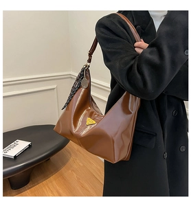 Brown patent leather hobo bag with metal triangle logo and charm, worn by model