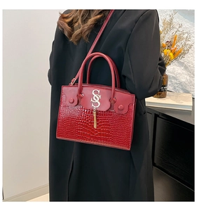 Close-up of red crocodile embossed leather handbag with metal logo and tassel details