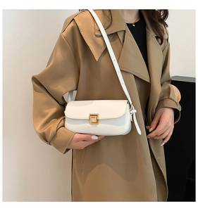 Nahaufnahme der weißen Leder-Umhängetasche mit Goldschnalle am Model im Trenchcoat