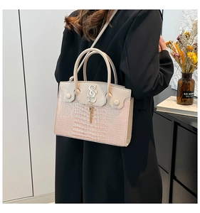 Detail of pink faux crocodile leather handbag with metal S-logo and fringe tassel charm