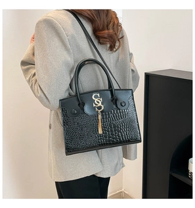 Detail of black tote bag featuring crocodile texture, gold SS logo, and metallic tassel