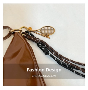 Detail of brown leather bag featuring gold tennis racket pendant and woven strap