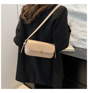 Détail d'un petit sac bandoulière beige avec boucle dorée porté sur une veste noire
