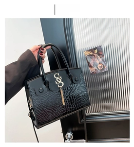 Detail of black crocodile pattern faux leather handbag with golden metal logo and tassel