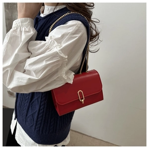 Borsa a tracolla in pelle rossa con fibbia dorata abbinata a un maglione blu a trecce