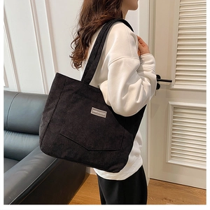 Detail view of black corduroy tote bag with textured fabric and front pocket on shoulder