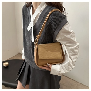 Detail of tan shoulder bag featuring woven texture flap and decorative knot on strap