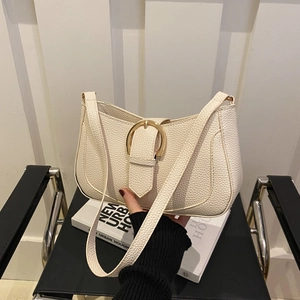 Chic cream leather hobo shoulder bag with a large gold buckle on a minimalist chair