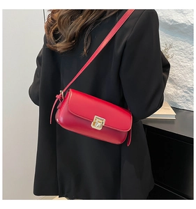Détail du sac bandoulière en cuir rouge avec fermoir doré porté sur un blazer noir