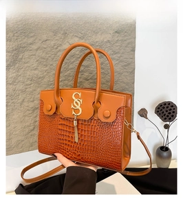 Detail of crocodile embossed leather handbag in brown with gold hardware and tassel