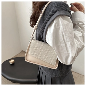 Close-up of cream shoulder bag featuring woven texture flap and minimalist sleek design