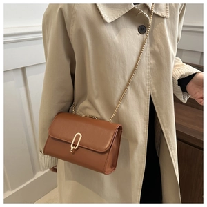 Borsa a tracolla marrone in ecopelle con catena dorata indossata su un trench kaki