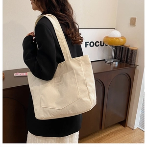 Detail of cream corduroy tote bag with front pocket and XINRUI GOOD text shown on shoulder