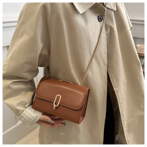 Dettaglio borsa a tracolla in pelle marrone con fibbia dorata su trench beige