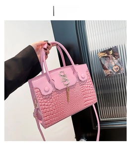 Detailed macro view of pink crocodile embossed leather with gold S-logo and fringe tassel