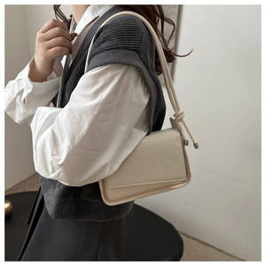 Detail of cream shoulder bag featuring woven texture and unique knotted strap design