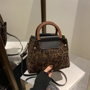 Fashionable leopard print handbag with wooden handles and leather flap on a mirror background
