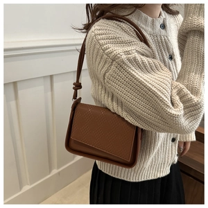 Detail of a brown shoulder bag featuring textured woven flap and elegant knot strap detail