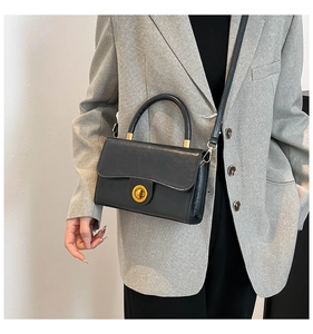 Detail of a chic black crossbody bag with gold buckle on a model in a grey blazer