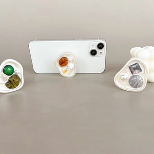 Dettaglio del supporto per cellulare con gemme colorate e perle su base bianca
