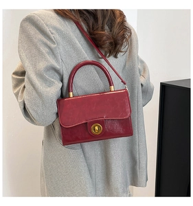 Détail du sac en cuir bordeaux avec fermoir doré porté avec un costume gris