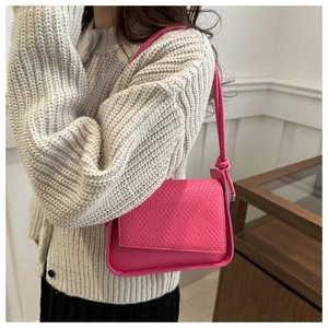 Detail of hot pink shoulder bag with woven texture and knotted strap on white knitwear