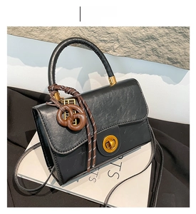 Detail of black leather handbag with gold twist lock and pretzel charm on textured rock