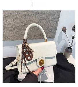 Detail of white square crossbody bag featuring a metal twist lock and woven rope pendant