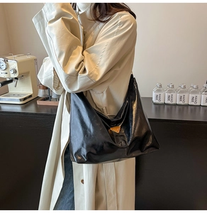Detail of glossy black hobo bag texture with metallic logo on a beige trench coat
