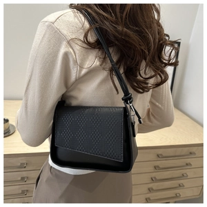 Macro detail of black textured flap on a minimalist crossbody bag with metal buckle