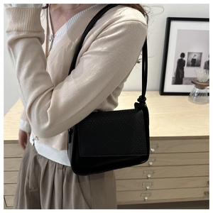 Close-up of black square bag featuring woven flap detail and knotted shoulder strap strap