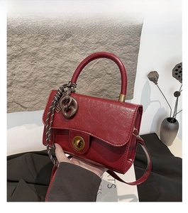 Detailed close-up of dark red faux leather texture and vintage metal lock on handbag
