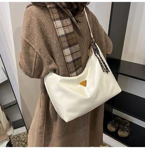 Detail of off-white semi-moon shoulder bag with metal triangle plaque on a brown coat