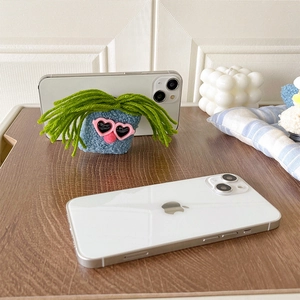 Funny plush blue doll phone grip with pink heart sunglasses on a wooden desk