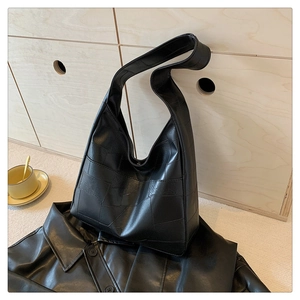 Detail of black leather hobo bag featuring quilted stitching on a minimalist wooden background