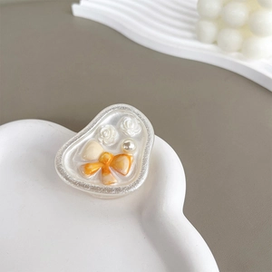 Close-up of heart-shaped phone grip with rose relief, pearl, and bow on a ceramic plate