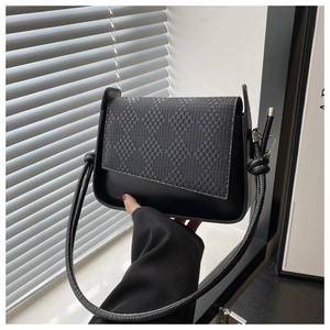 Detail of black woven texture flap and cylindrical rope shoulder strap on a handbag