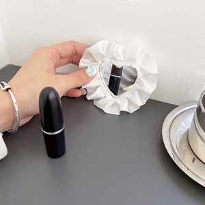 Detailed view of heart-shaped makeup mirror with white ruffled lace edge and silk texture