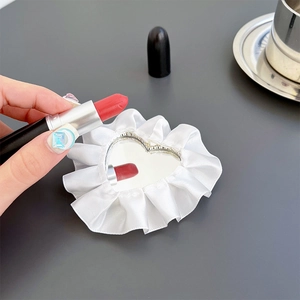 Macro detail of heart-shaped makeup mirror with white ruffled fabric edge and reflection